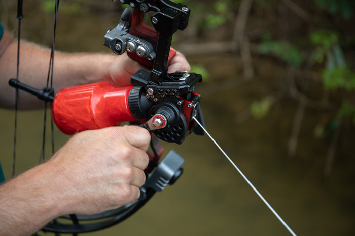 Cajun Bowfishing Winch Pro Reel, bowfishing reel, attached to a Cajun bowfishing bow being used on a lake.